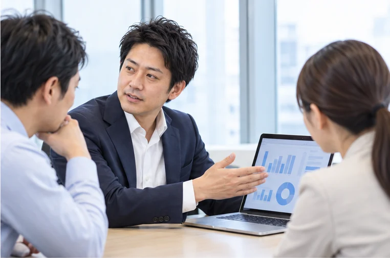 会議室で、お客さまにノートパソコンを見せながら説明する営業の社員